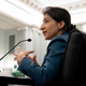 Lina Khan holds her hands in front of me as she speaks in a microphone to her left.
